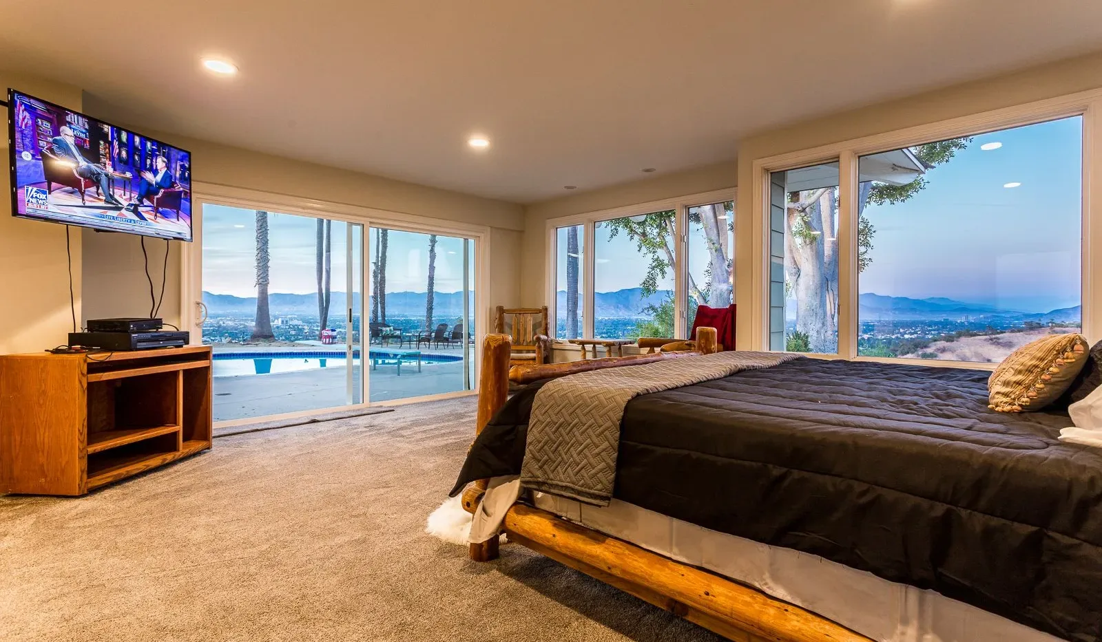 Dormitorio con una cama grande junto a ventanas con vistas a una piscina y al agua.
