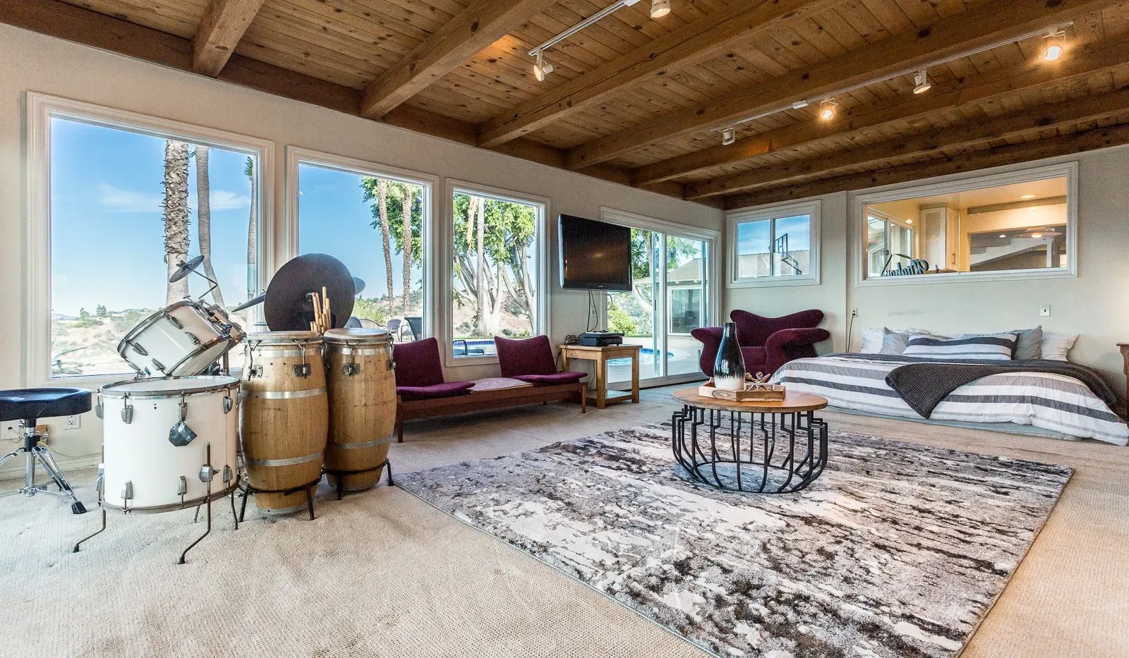 A bright living room with a drum set, seating, and a large patterned rug.