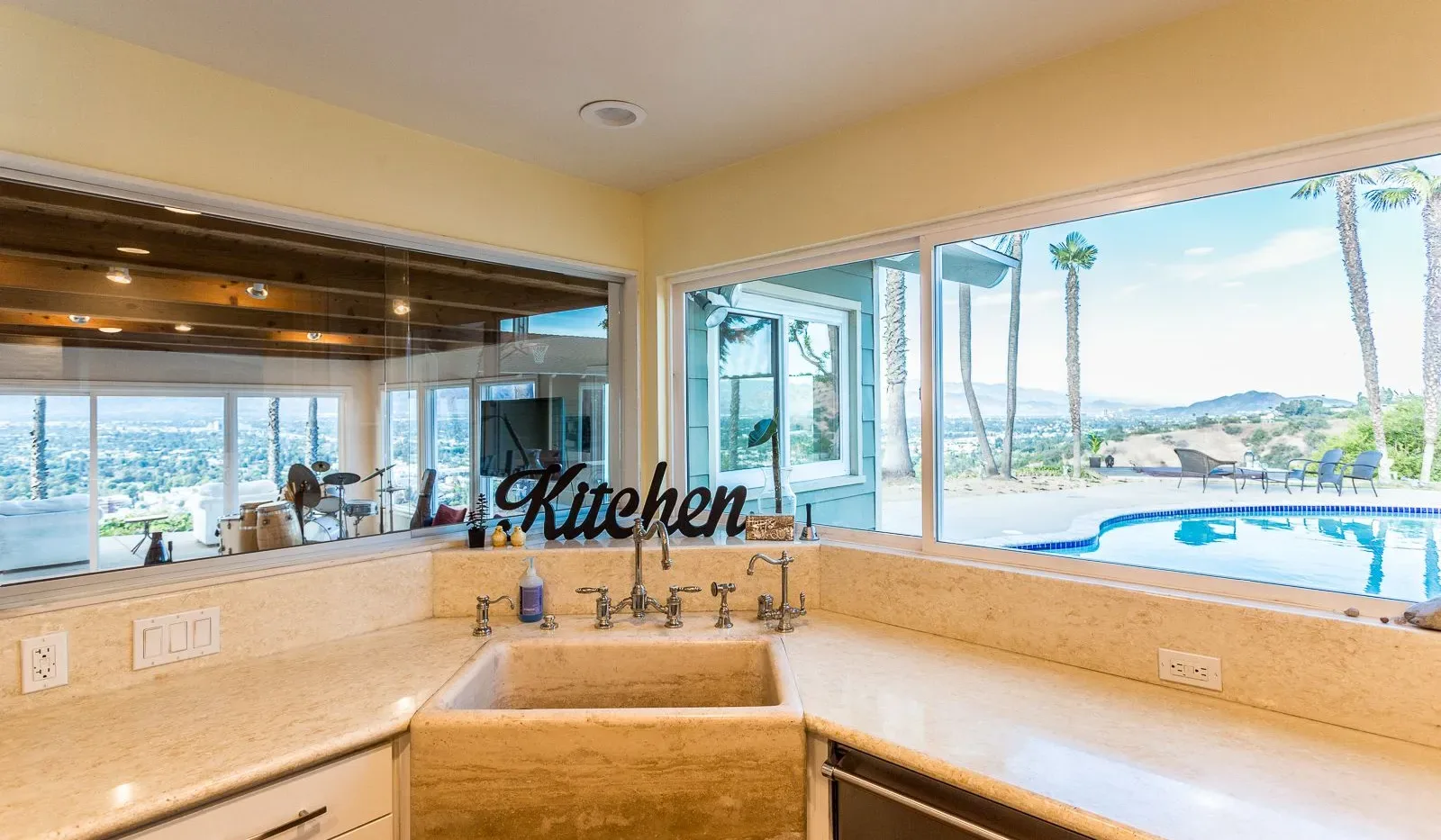 Una cocina con fregadero y amplias ventanas con vistas a una piscina y un paisaje costero.