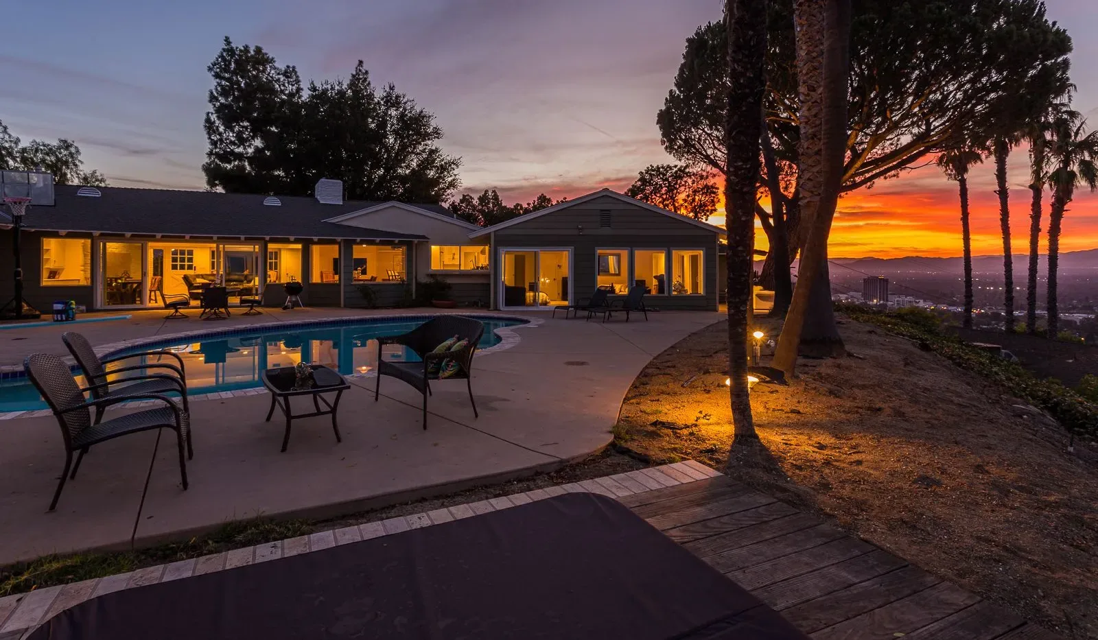 Un patio junto a la piscina, al lado de un edificio bajo, mira hacia las colinas al atardecer.