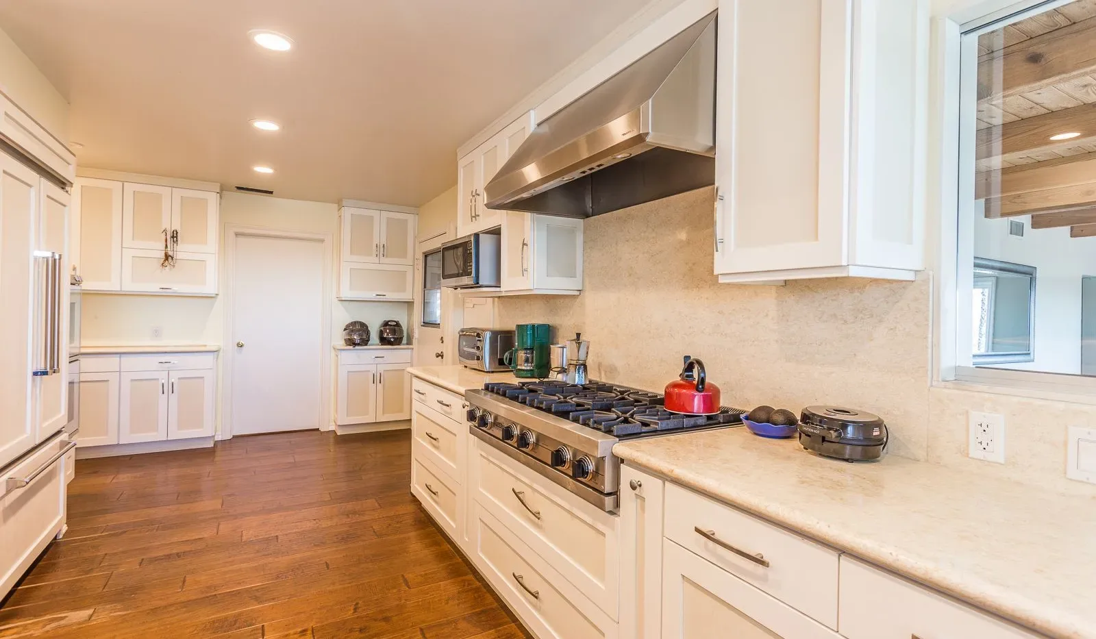 Una cocina luminosa con gabinetes blancos, una estufa grande y piso de madera.