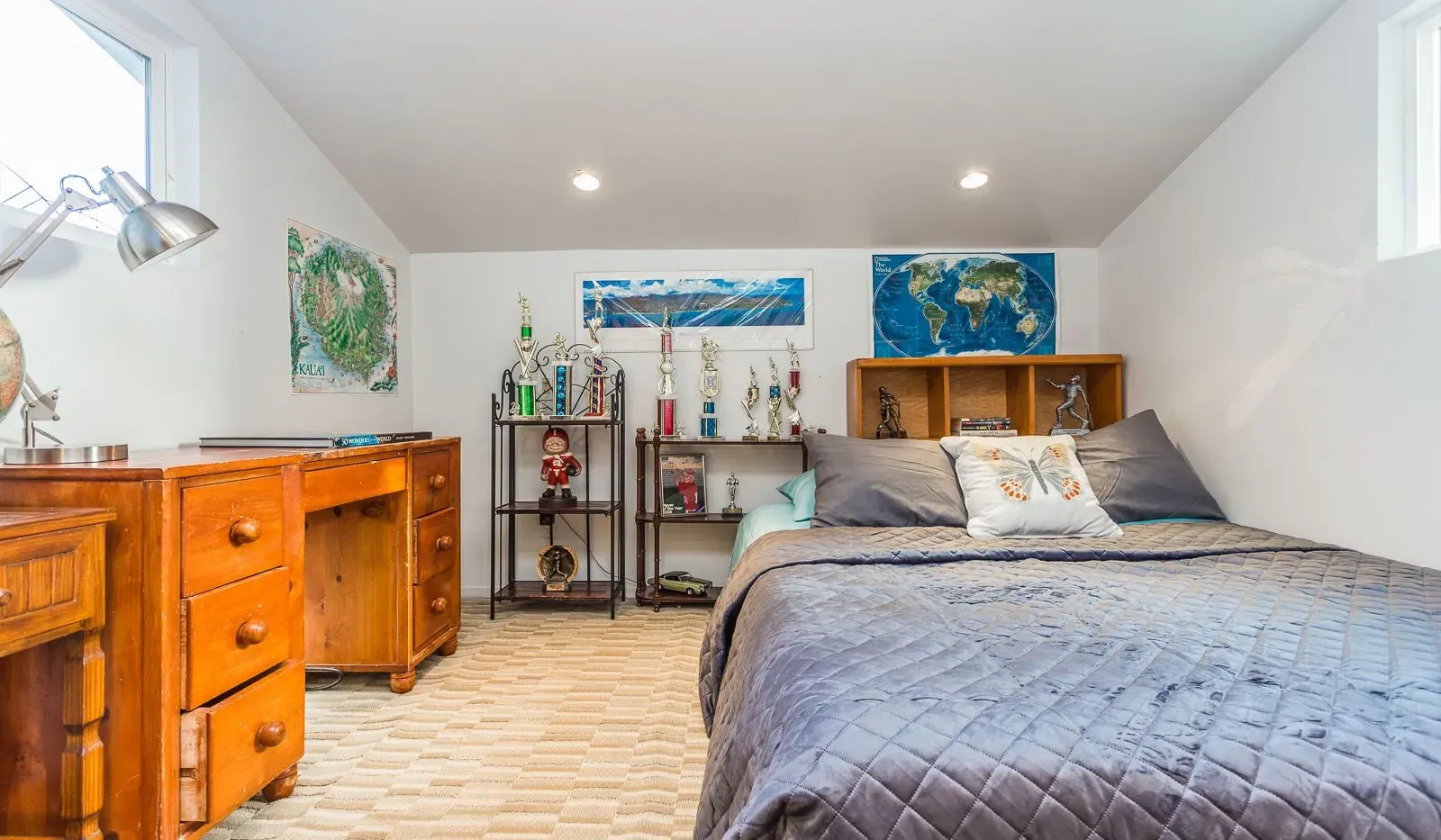 Un dormitorio con una cama grande, una cómoda de madera y estantes con trofeos.