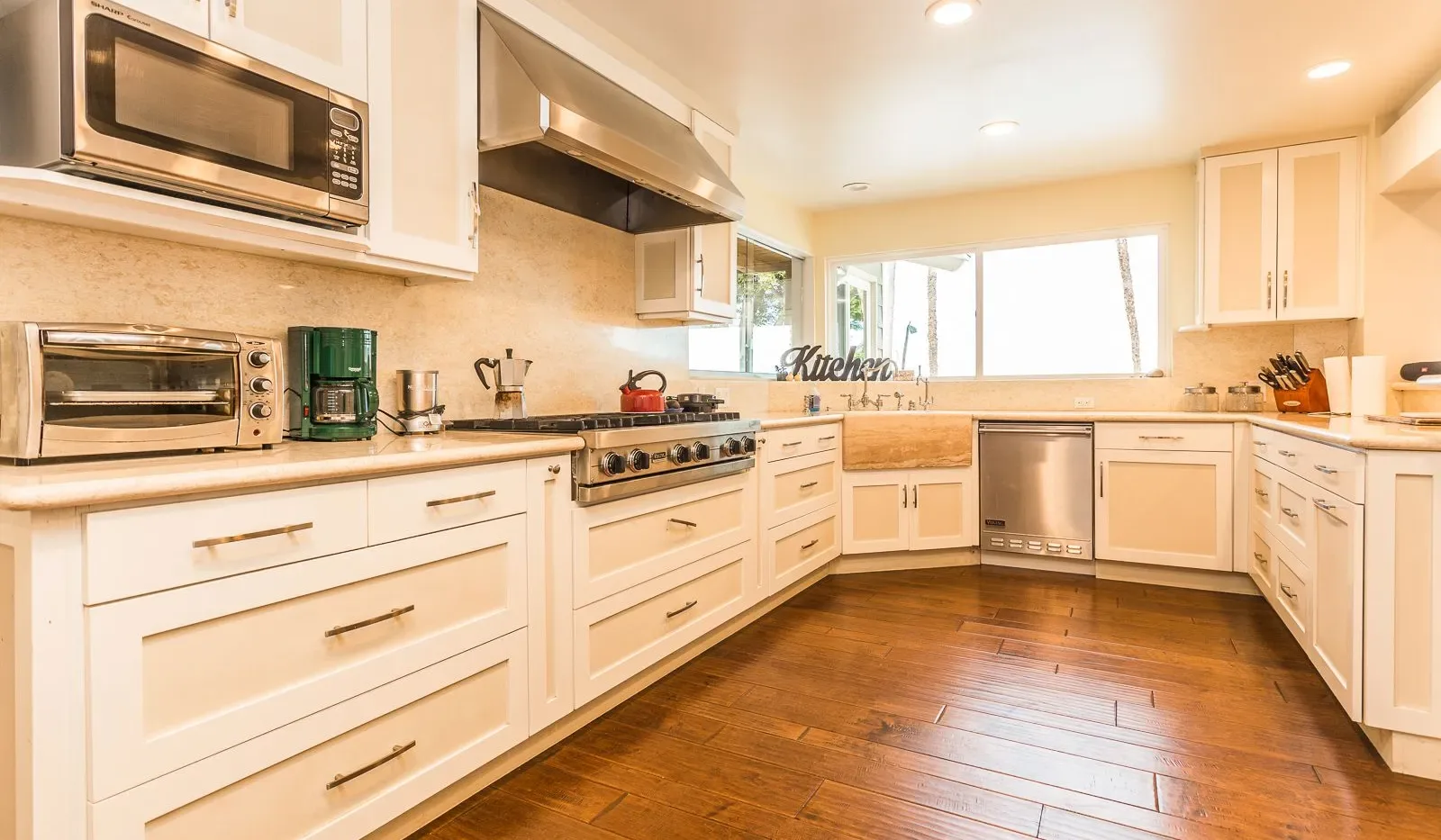 Una cocina luminosa con gabinetes blancos, electrodomésticos de acero inoxidable y piso de madera.