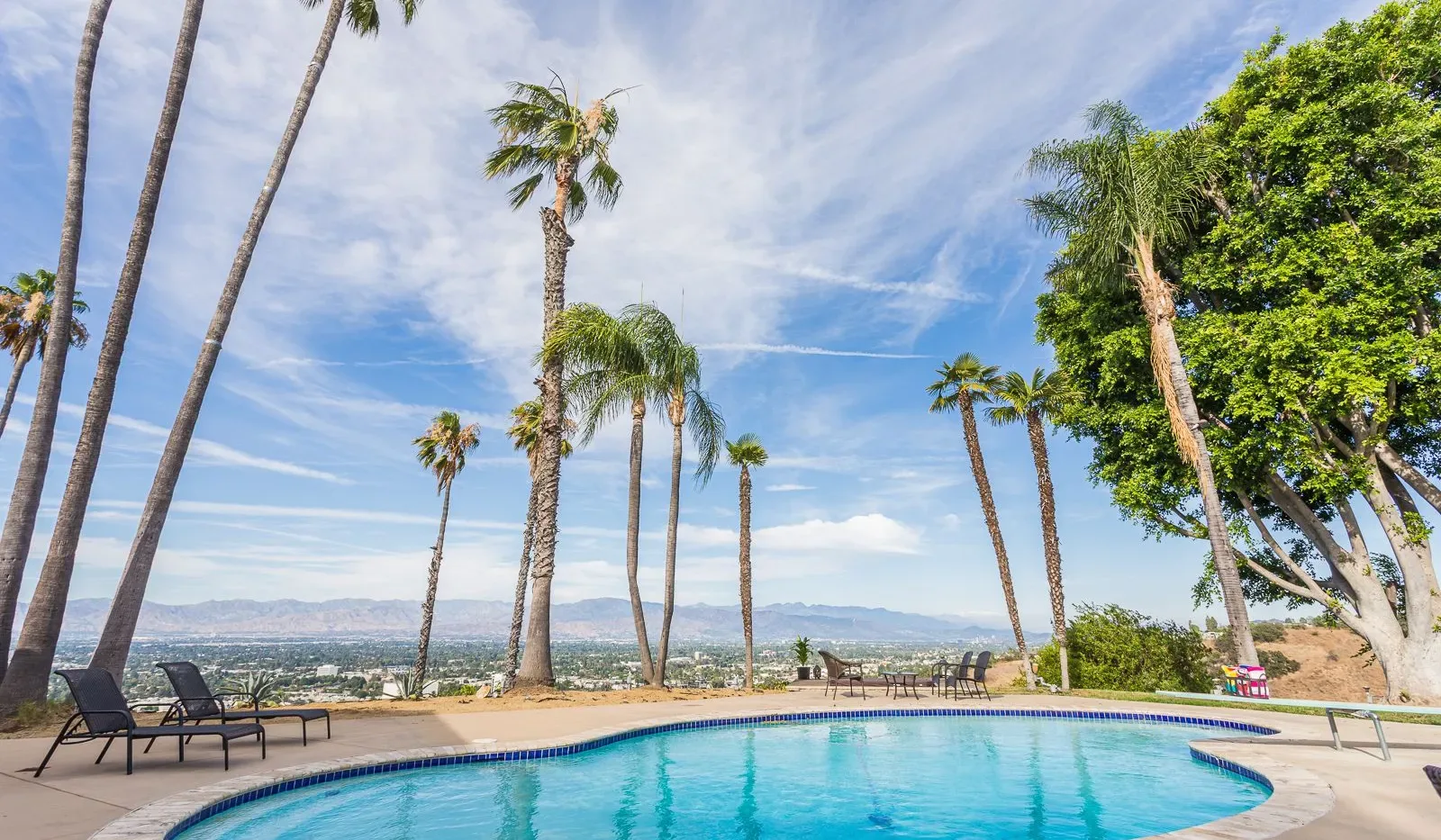 Una piscina está rodeada de palmeras, con montañas a lo lejos.