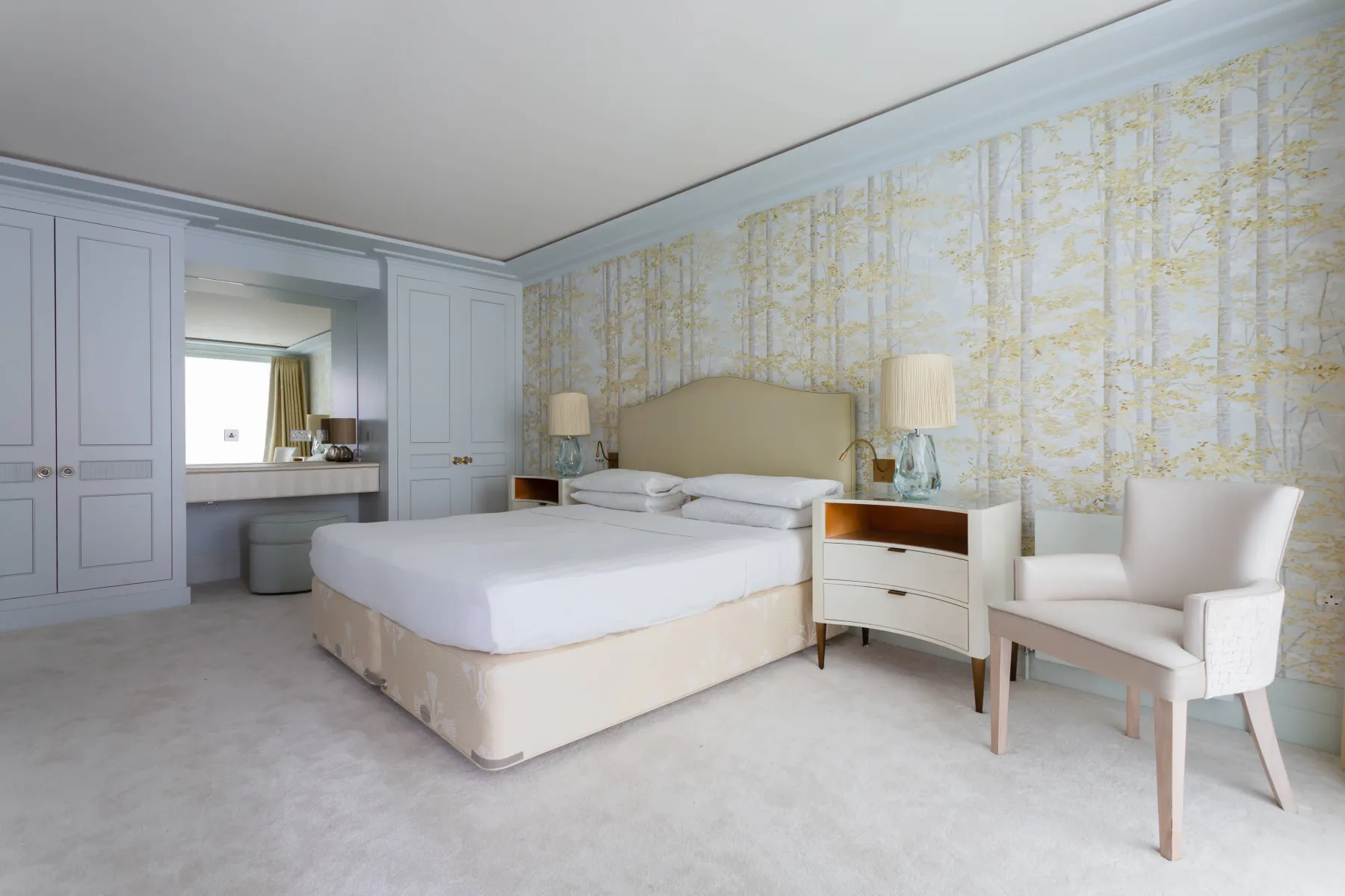 A bedroom with a large bed and a light upholstered chair.