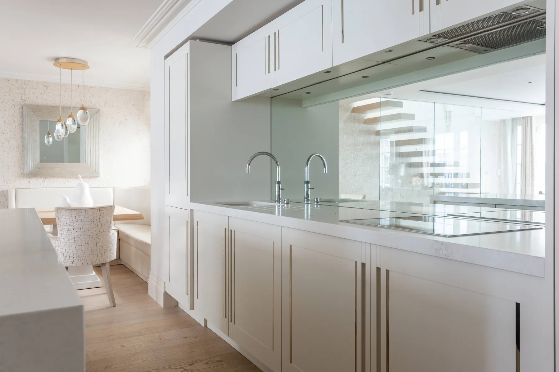 Una cocina luminosa con gabinetes blancos, encimera y salpicadero de espejo.