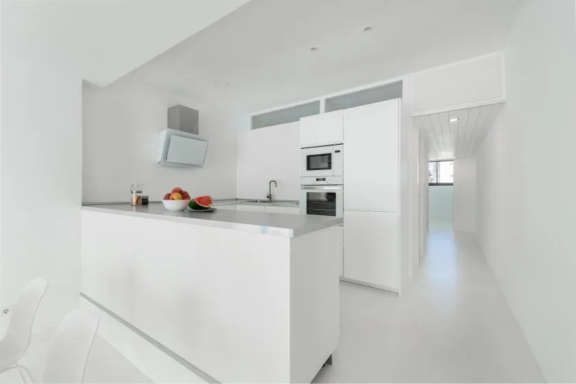 A bright white kitchen with a long island and built-in appliances.