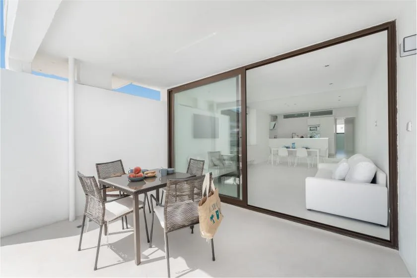 Un patio luminoso con mesa de comedor y asientos junto a una gran ventana de vidrio.