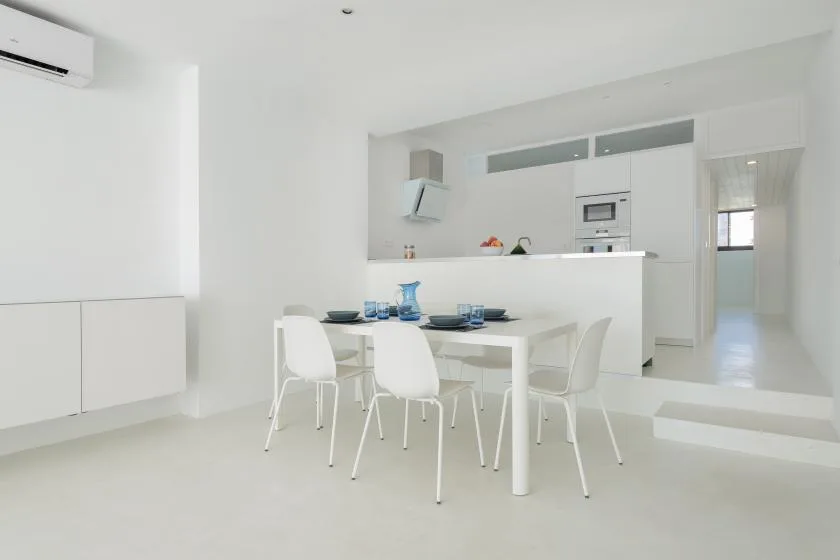 A bright dining area with a table and seating beside a white kitchen.