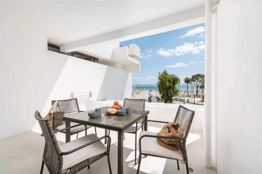 Una luminosa zona de comedor al aire libre con asientos tejidos y vistas al mar.