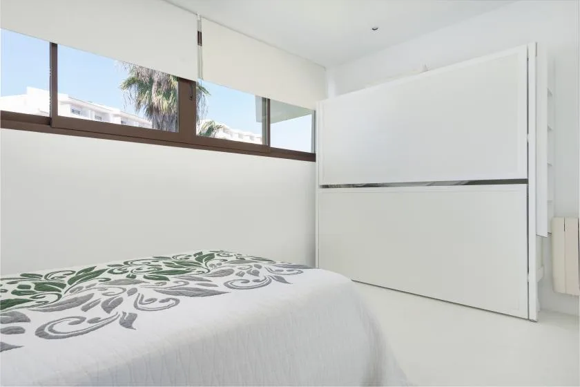 A bright bedroom with a patterned bedspread and a wide window.