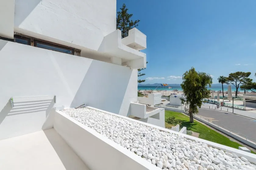 A white building terrace overlooks a coastal road and the sea.