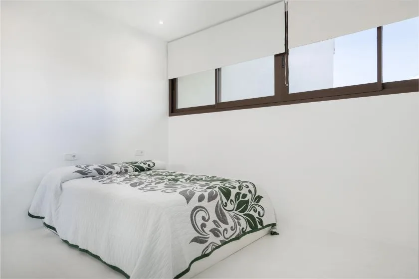 A bright bedroom with a bed covered in white bedding with dark floral patterns.