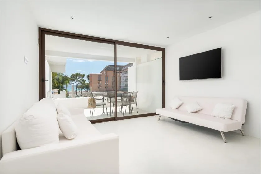 A bright living room with white seating and a large glass door opening onto a dining area.