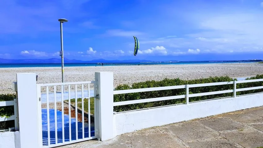 A white gate and fence overlook a sandy beach and blue sea.