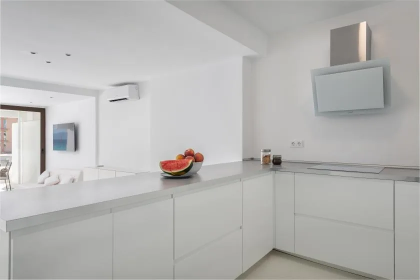 A bright white kitchen with a long counter and a bowl of fruit.