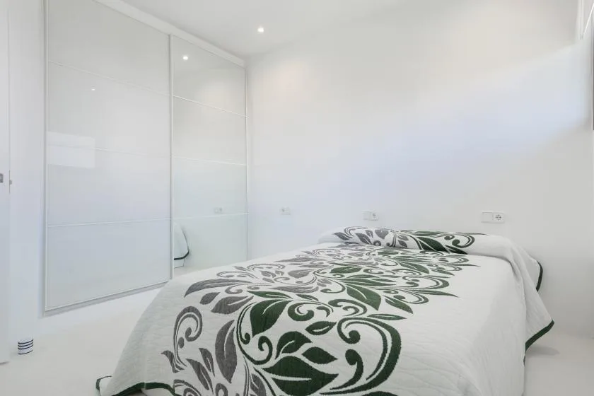 A bright bedroom with a bed covered in white bedding with dark green patterns.