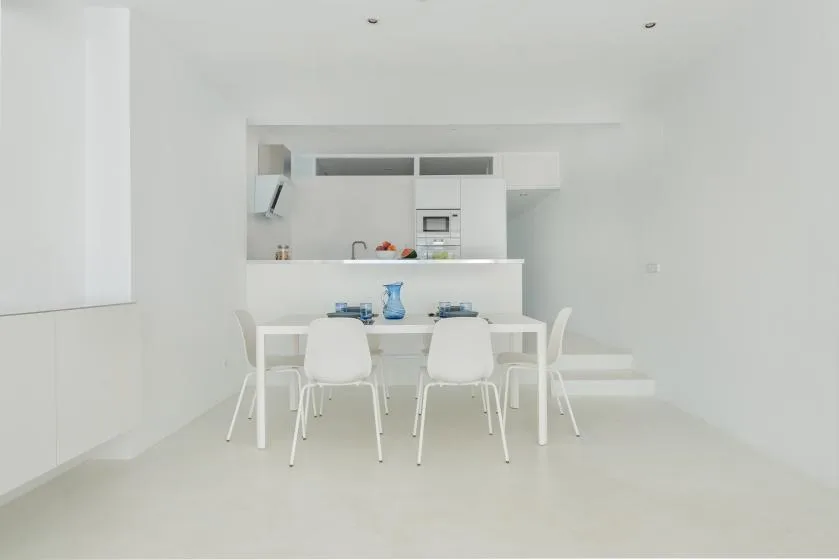 A bright white dining area with a table and chairs in front of a kitchen.