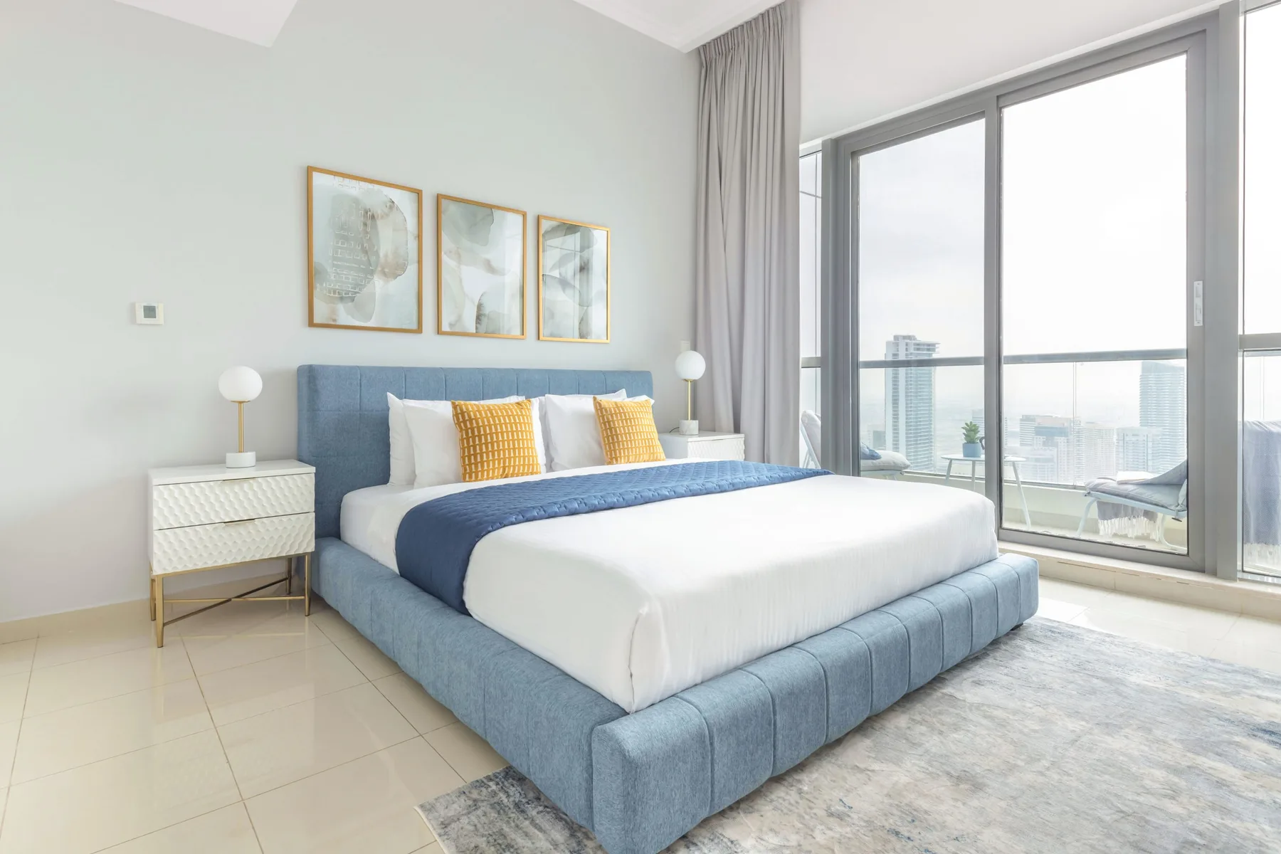 Un dormitorio luminoso con una cama azul junto a una ventana grande.
