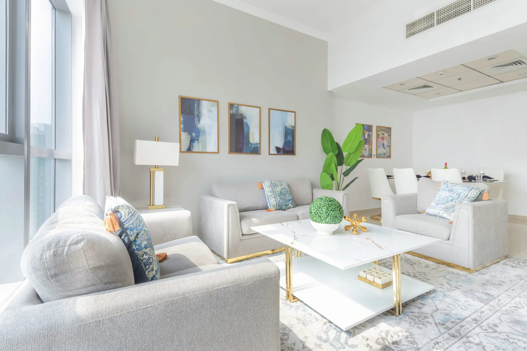 Una sala luminosa con asientos claros, una mesa de centro y grandes ventanas.