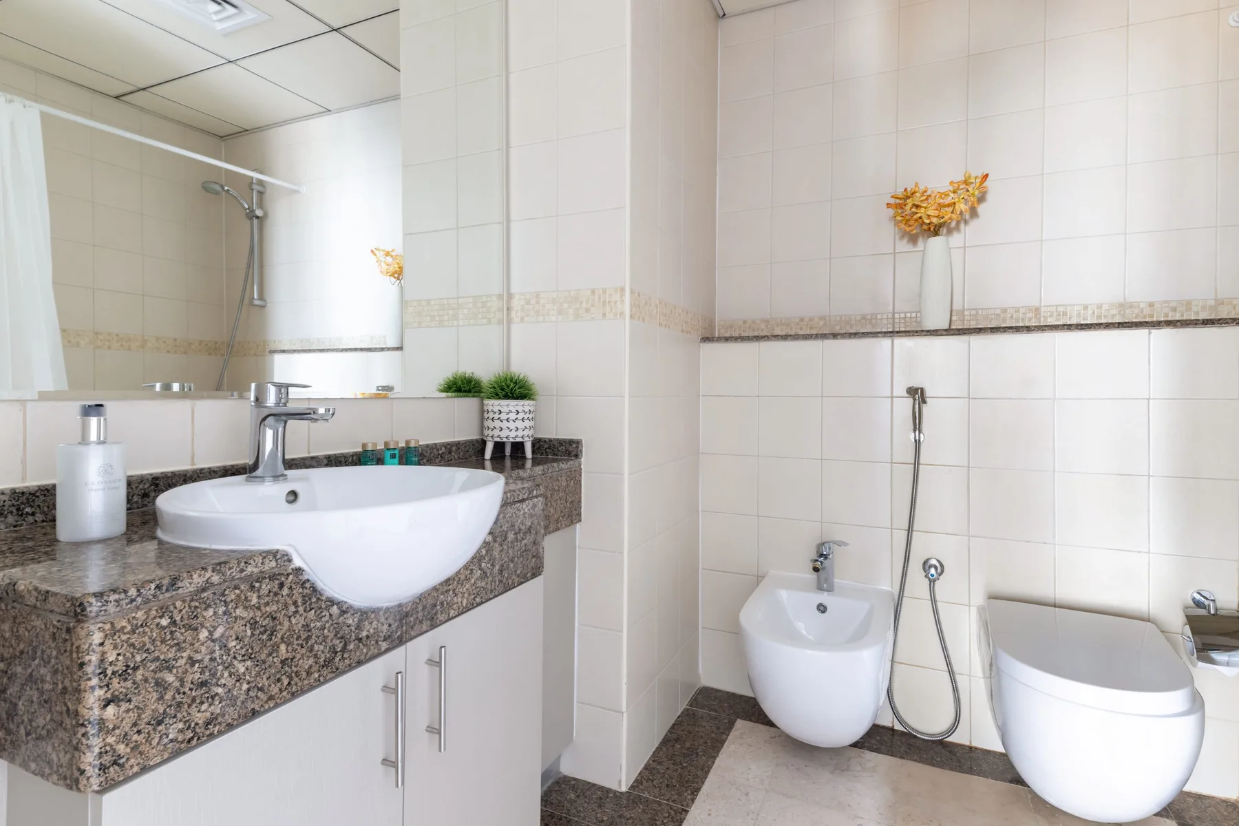 Un baño alicatado con lavabo, bidé, inodoro y ducha de mano.