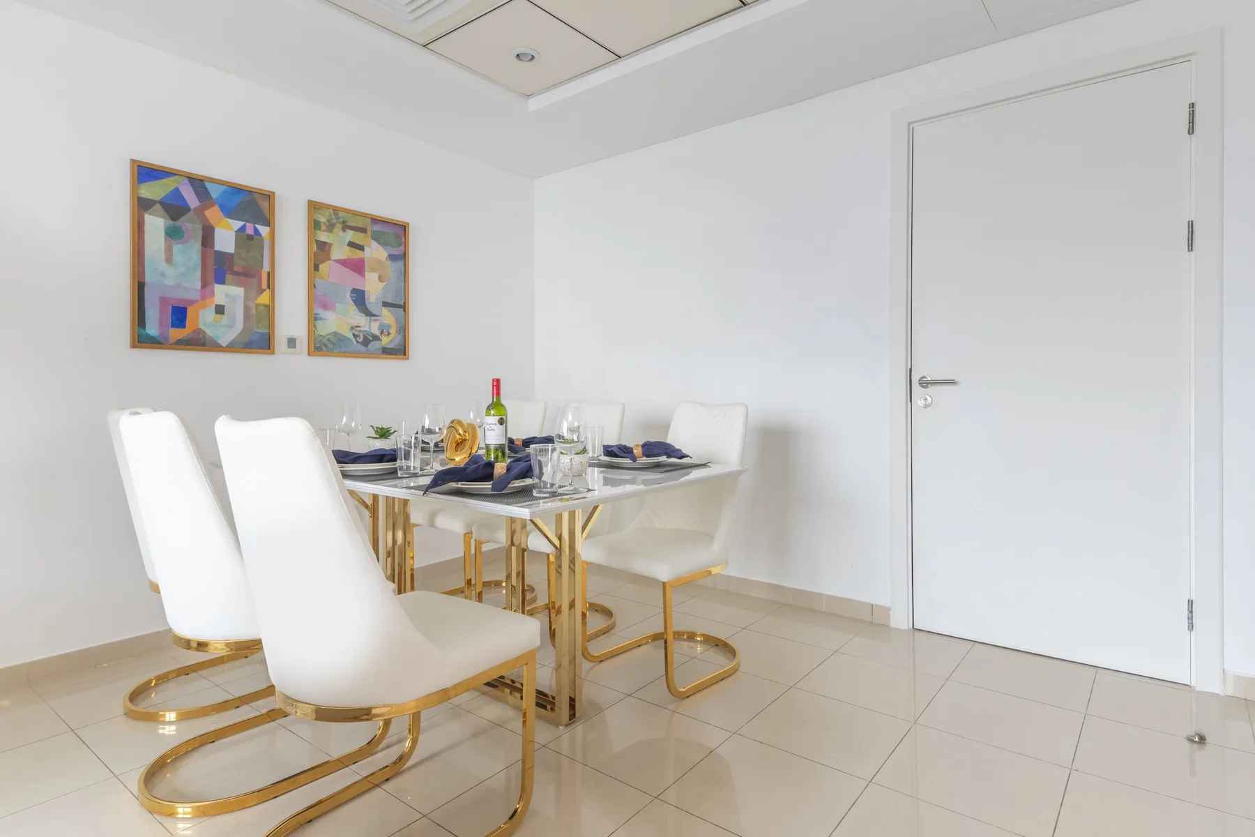 Un comedor luminoso tiene una mesa puesta y asientos blancos.
