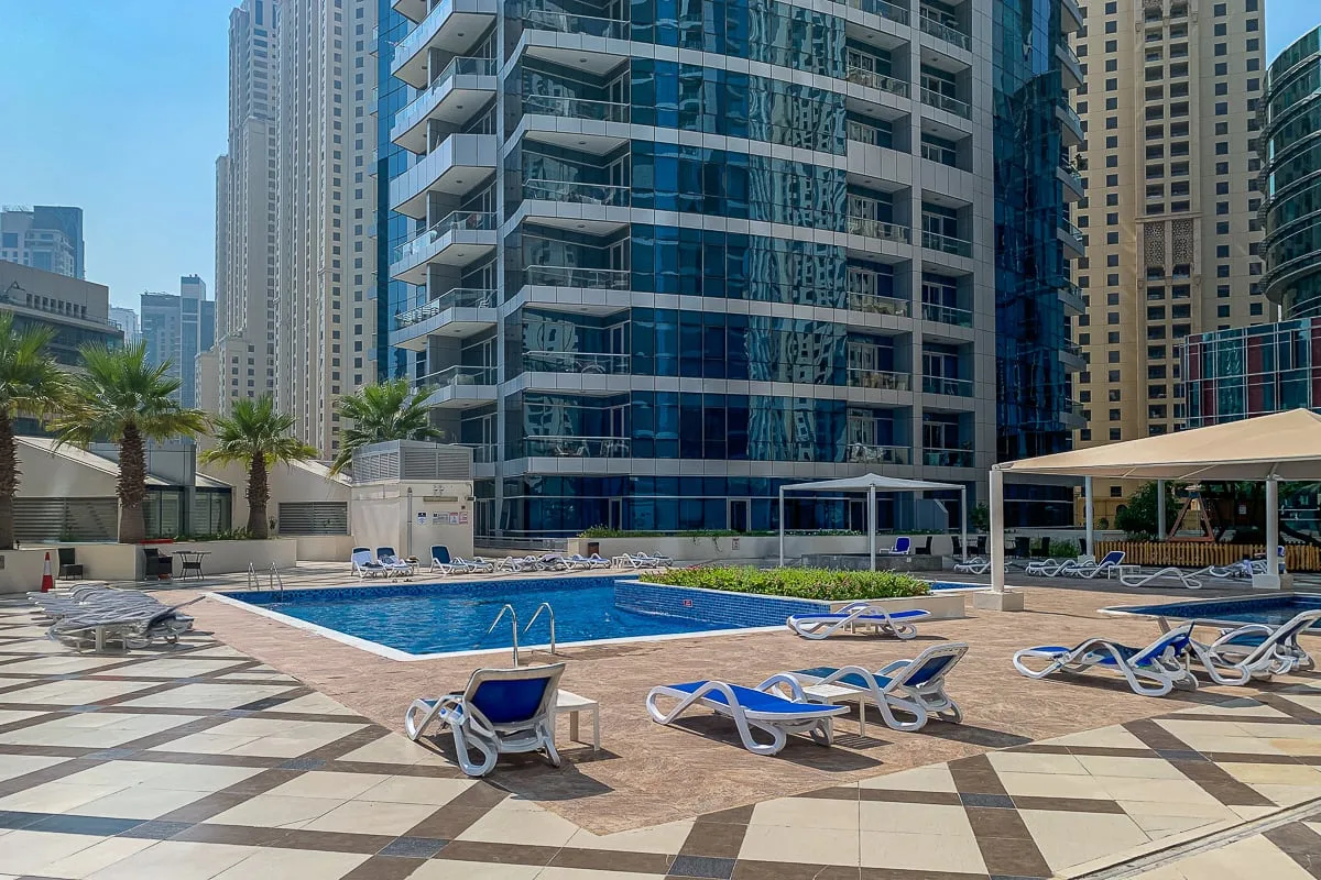 Una piscina exterior está junto a un edificio alto, con tumbonas alrededor de la terraza.