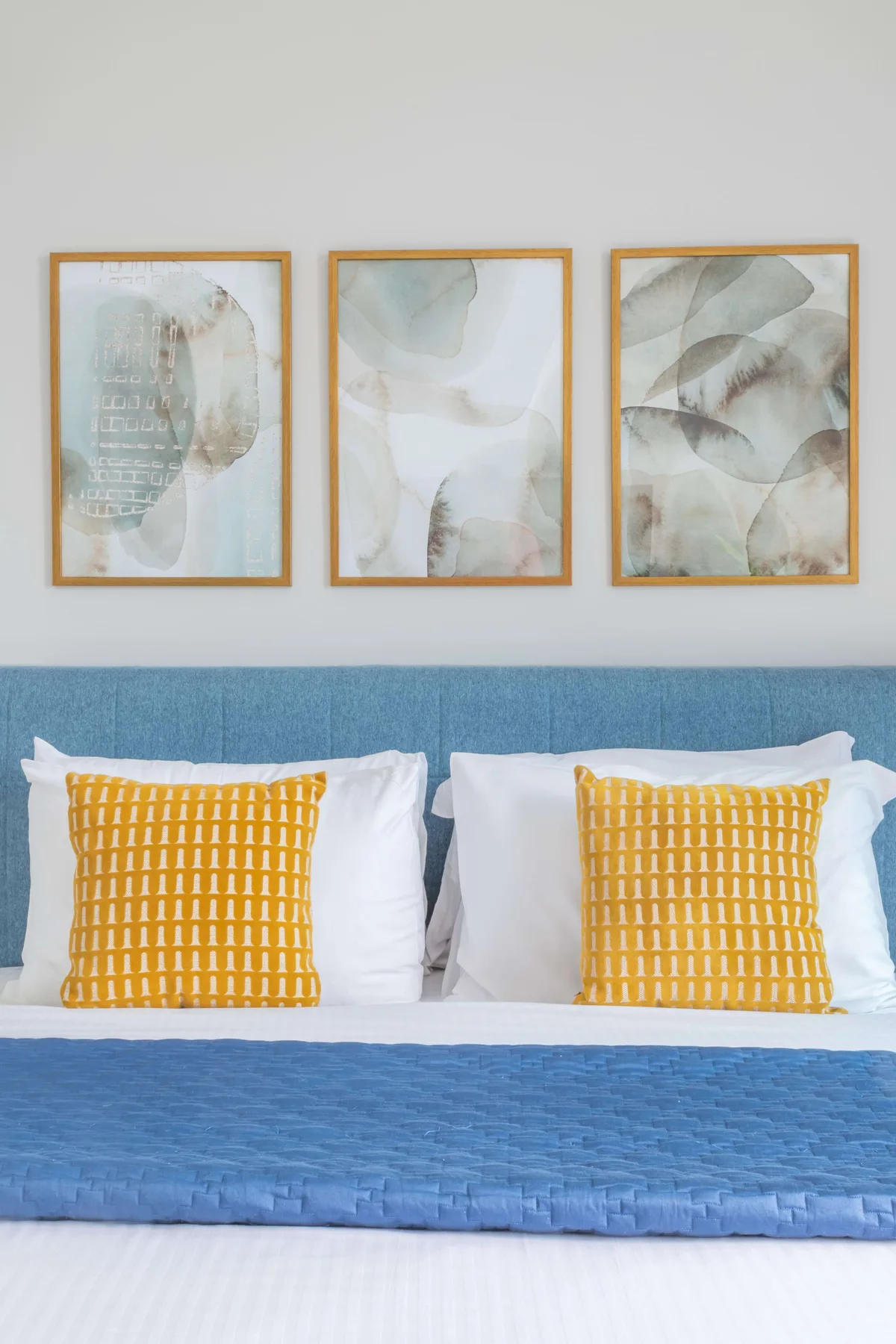Un dormitorio con una cama azul, almohadas blancas y cuadros sobre el cabecero.