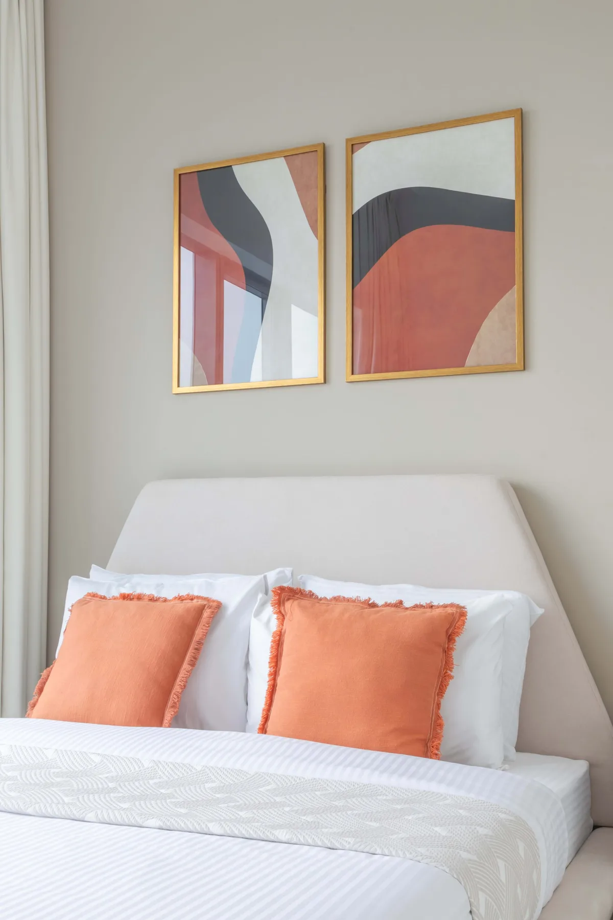 Un dormitorio con una cama bien arreglada y dos láminas abstractas enmarcadas encima.
