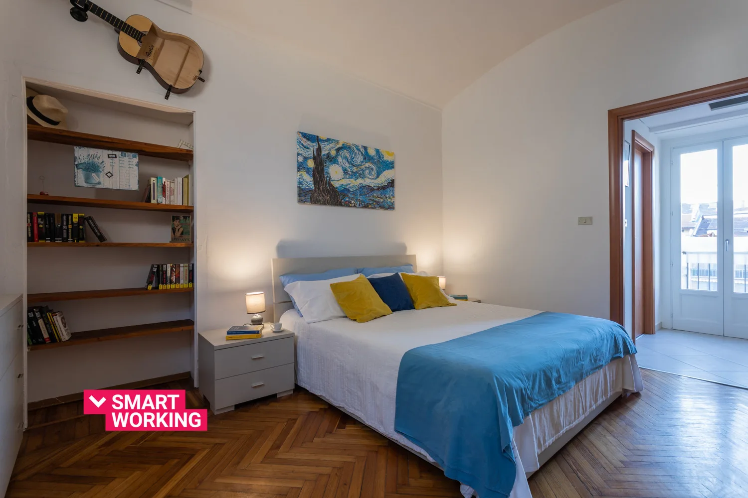 A bedroom with a bed dressed in white and blue bedding beside a bookshelf.