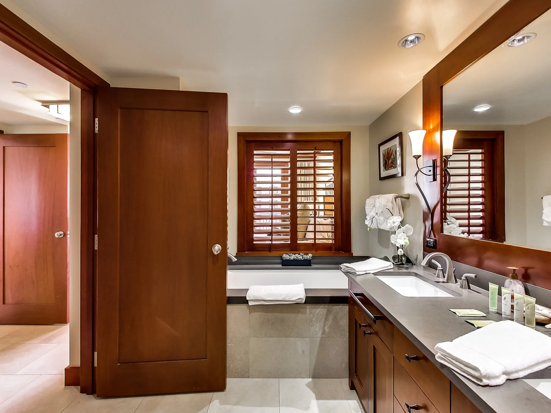 A bathroom vanity with a sink, large mirror, and shuttered window.