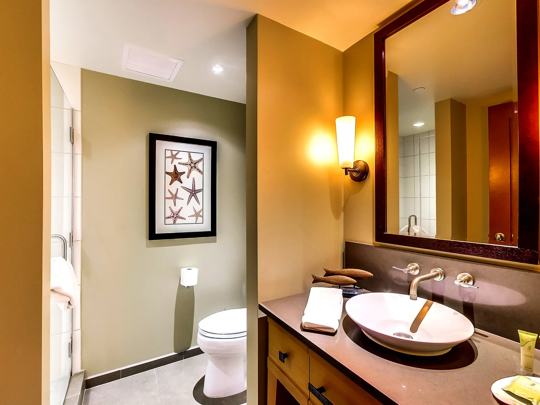 A bathroom vanity with a vessel sink and a mirror beside the toilet.