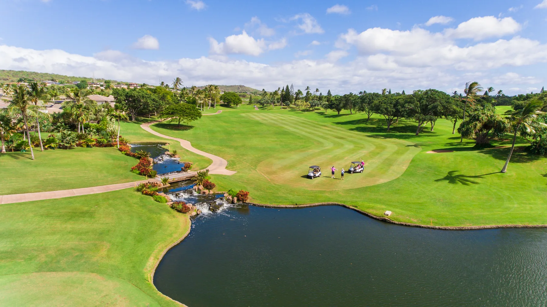A landscaped golf course with a pond, curving paths, and scattered trees.