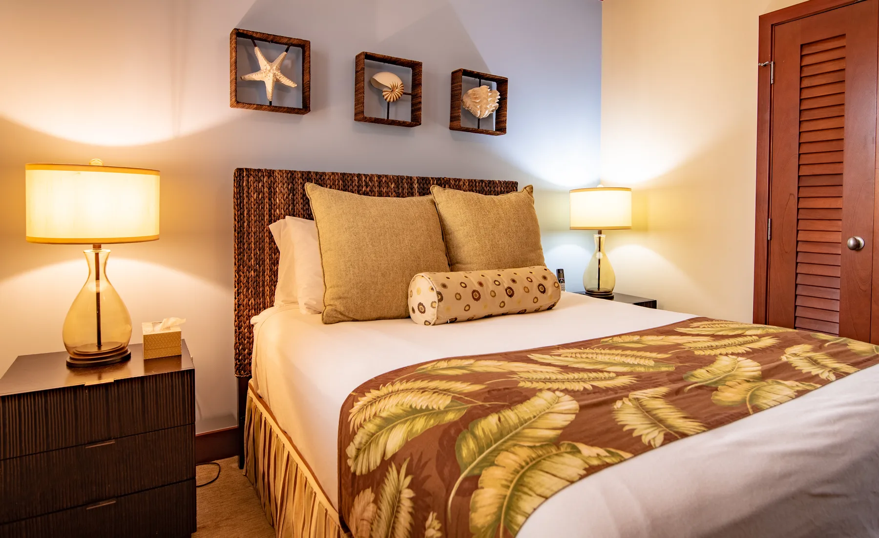 A bedroom with a neatly made bed, patterned bedding, and framed shell decorations.