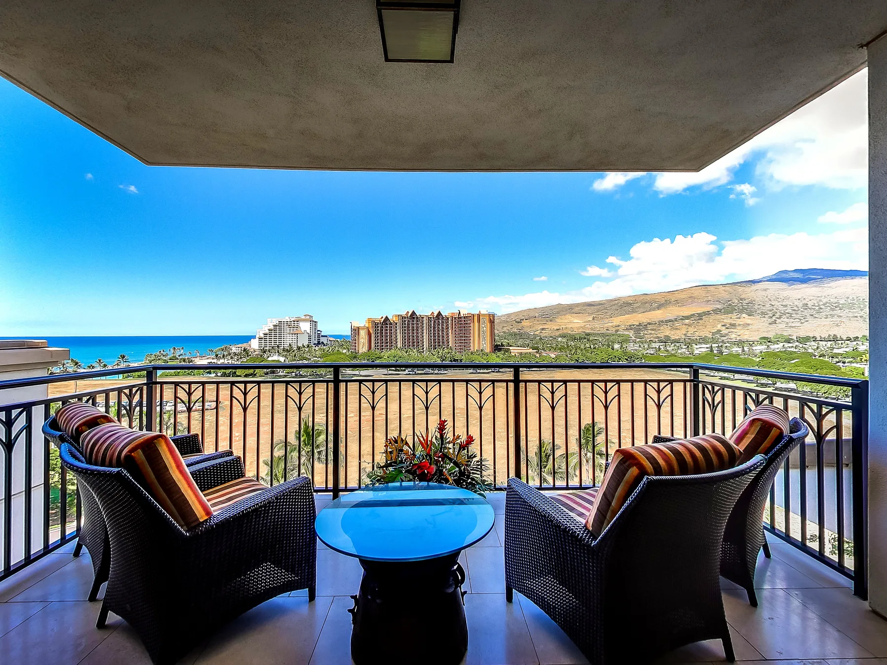 A balcony with seating overlooks the sea and a dry hillside.