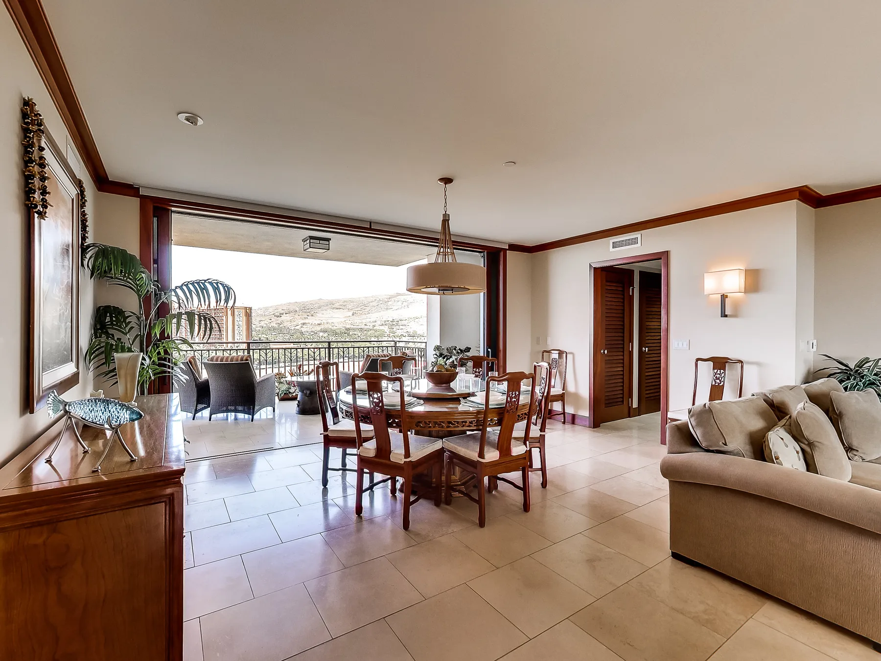 A dining and living area opens onto a balcony with a view of the hills.