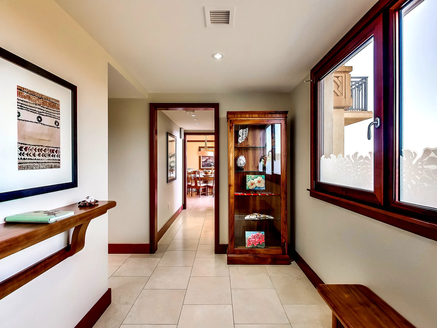 A bright hallway with tiled flooring, a display cabinet, and a large window.