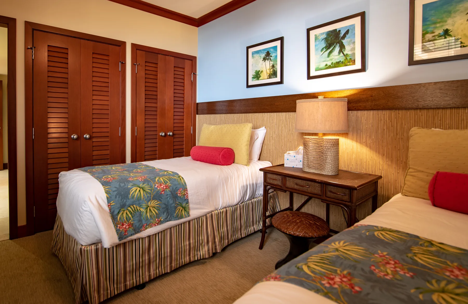 A bedroom with two beds, tropical-patterned bedding, and framed artwork on the walls.