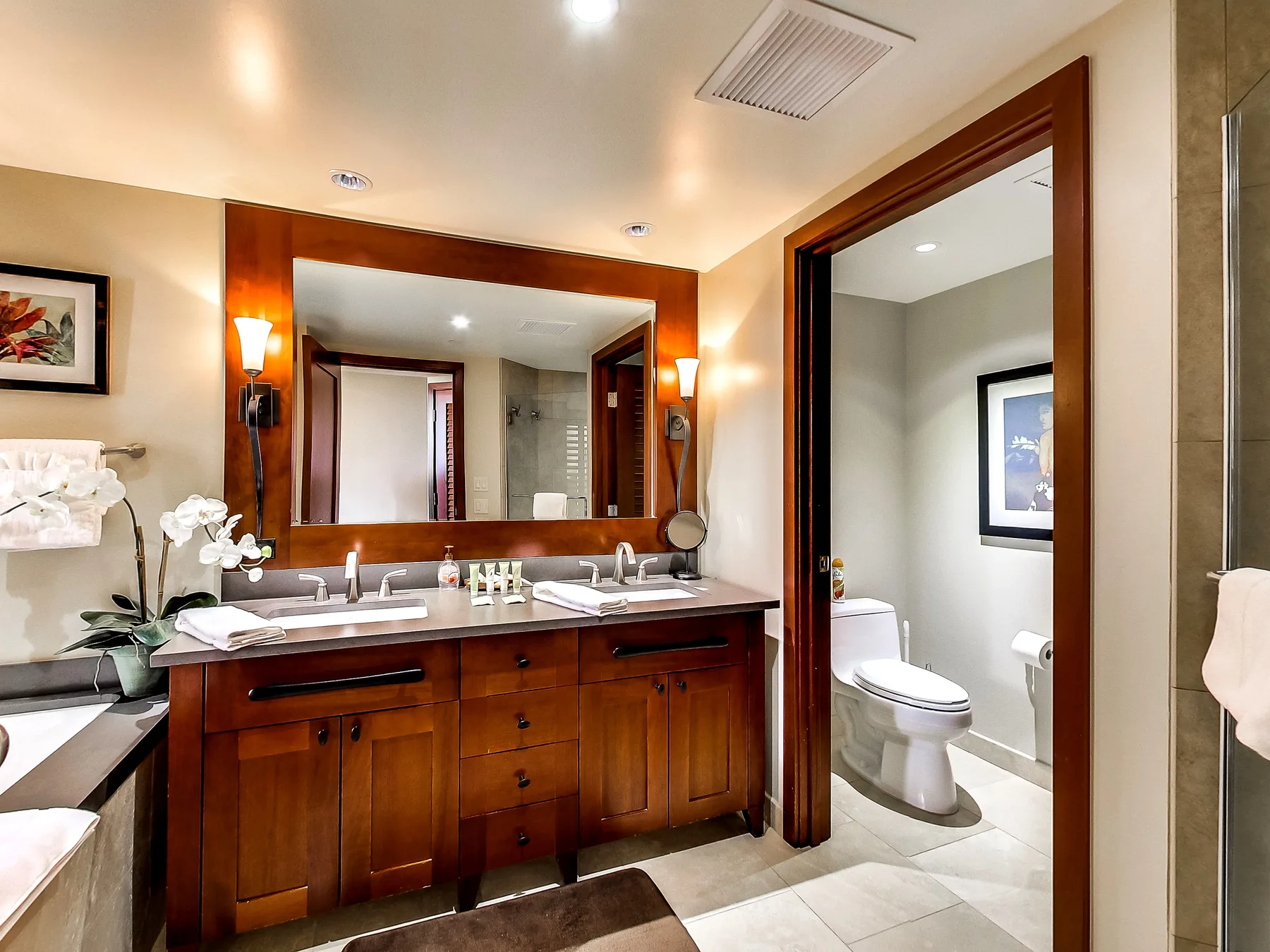 A bathroom vanity with a large mirror beside an open doorway to the toilet area.
