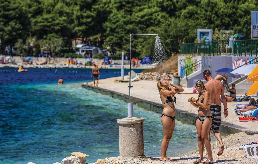 Una playa concurrida junto a aguas claras, con gente cerca de la orilla.
