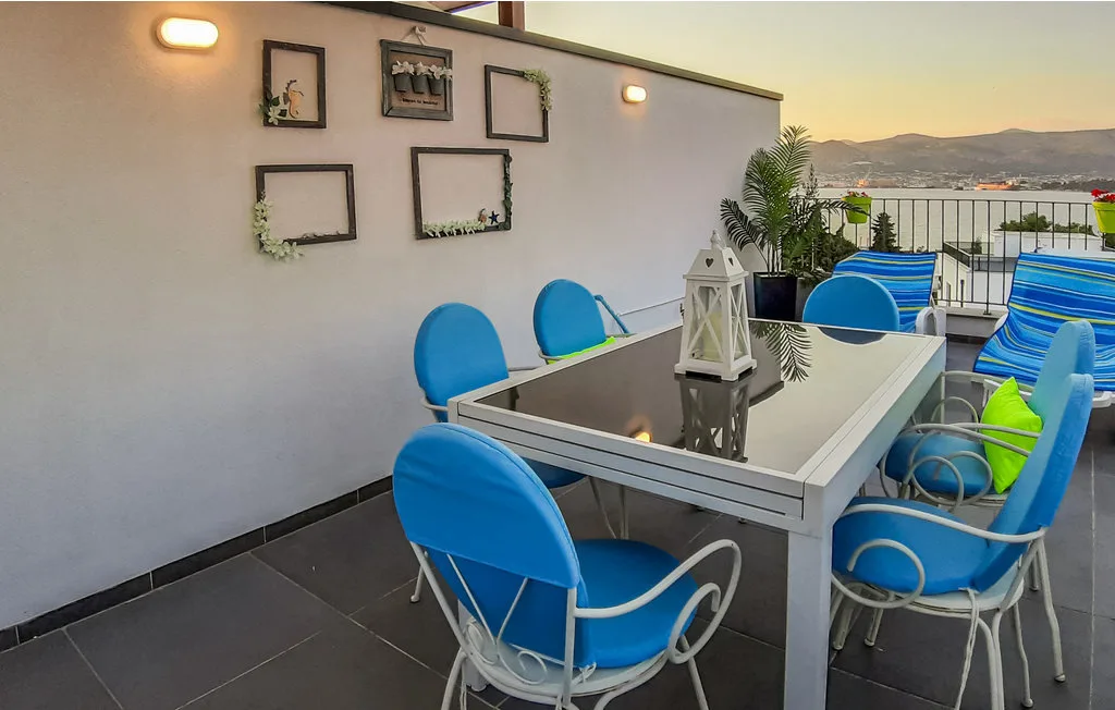 Una zona de comedor en la azotea con mesa de vidrio y asientos azules tiene vistas al paisaje.