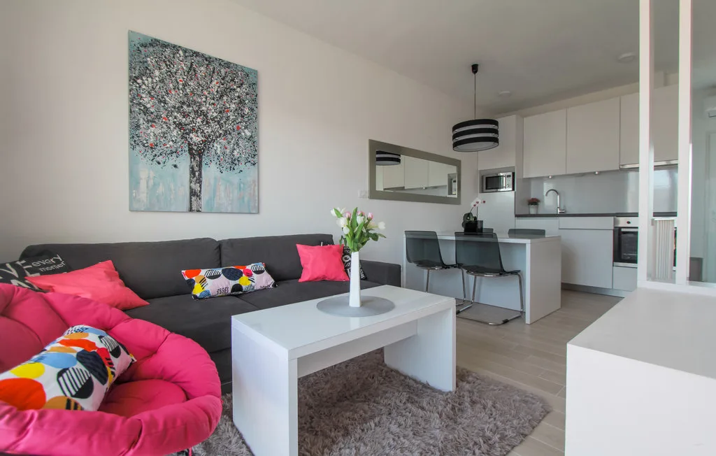 Una sala de estar se conecta con una cocina, con un sofá gris y una mesa de centro blanca.