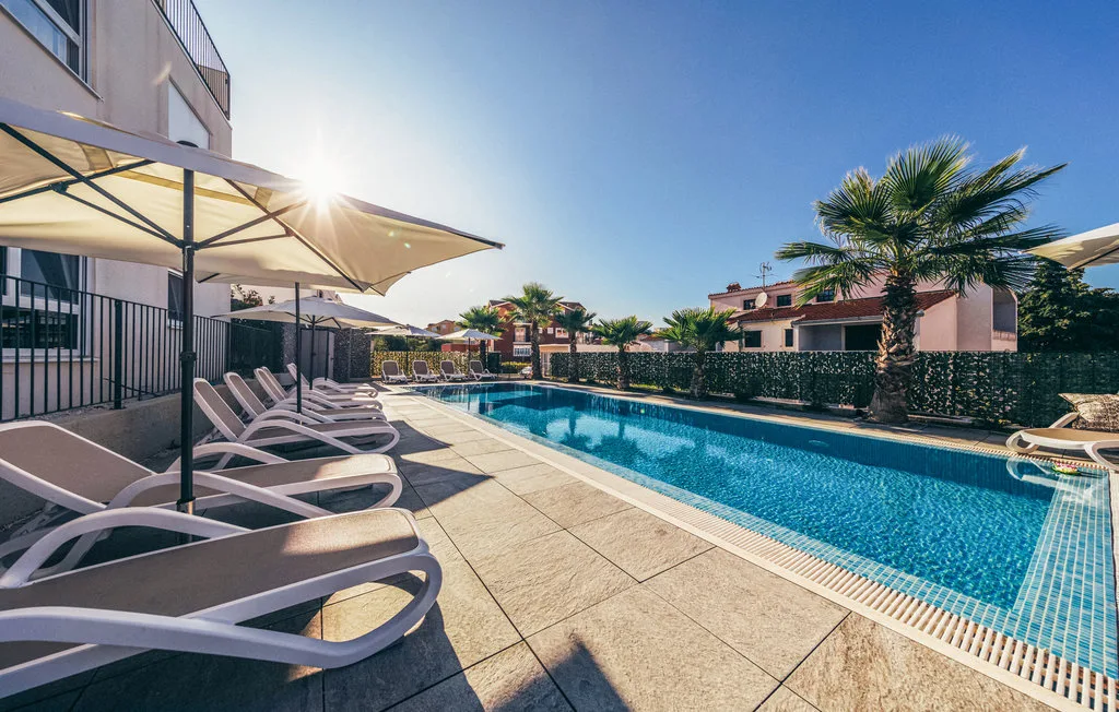 Una piscina al aire libre junto a asientos reclinables y una sombrilla grande.