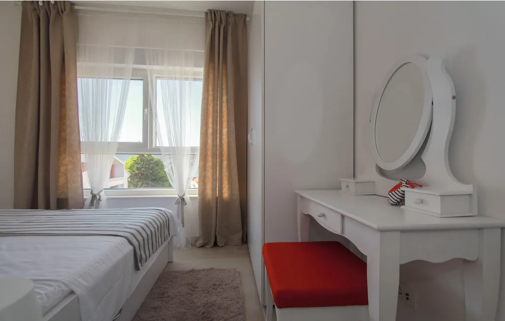 Dormitorio con una cama junto a un tocador y una ventana con cortinas.