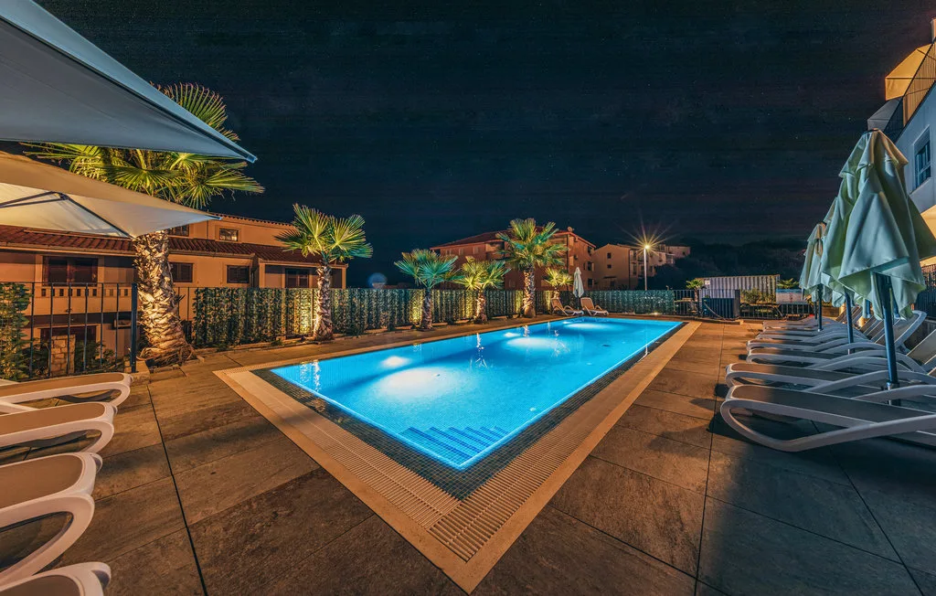 Una piscina iluminada está rodeada de asientos de descanso por la noche.