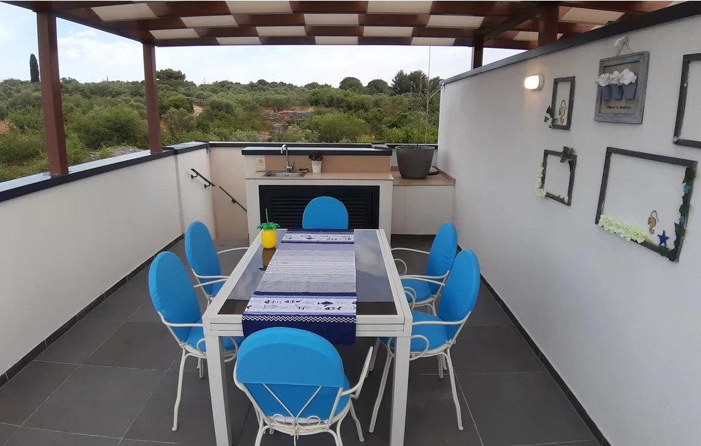 Una terraza cubierta tiene una mesa con sillas azules y vistas a la vegetación.