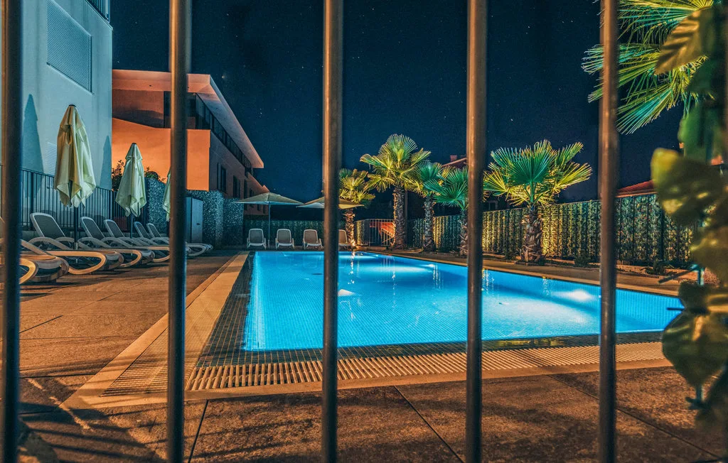 Una piscina iluminada de noche, con asientos y palmeras cerca.