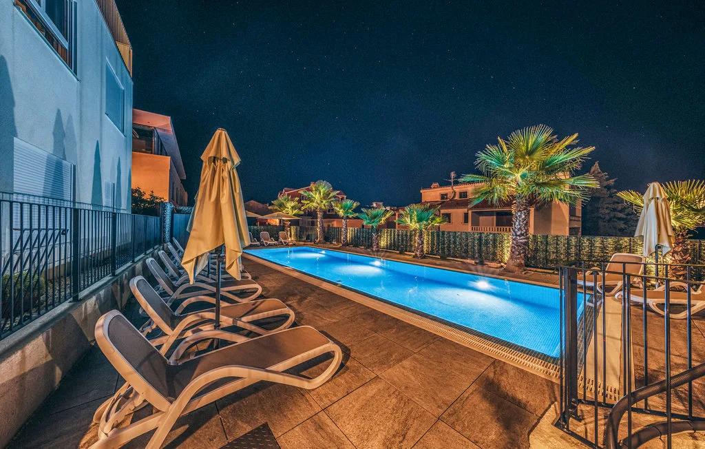 Una piscina exterior de noche está rodeada de asientos reclinables y palmeras.