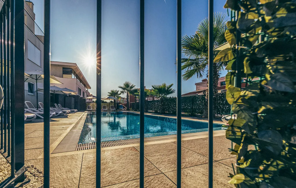 Una piscina al aire libre está junto a una terraza pavimentada y edificios cercanos.