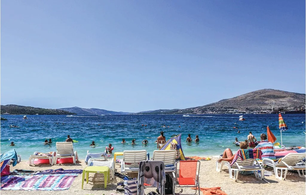 Una playa soleada con tumbonas coloridas, sombrillas y bañistas en el agua.